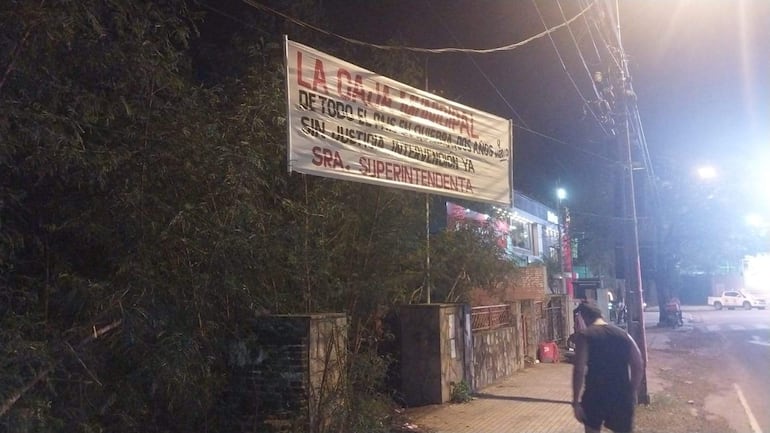 Carteles con reclamos a la Caja Municipal en microcentro de Asunción, y un hombre con camiseta sin mangas caminando por la acera.