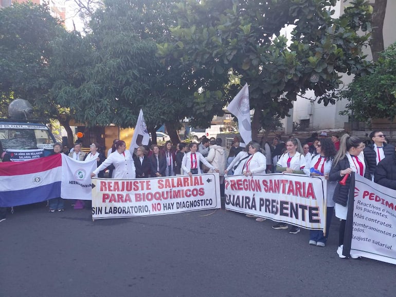 Bioquímicos sosteniendo pancartas que demandan reajuste salarial frente al Ministerio de Salud.