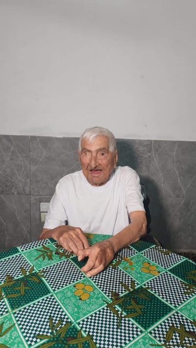 Canuto González, hombre mayor canoso, sonríe sentado frente a una mesa con mantel colorido en un hogar acogedor.