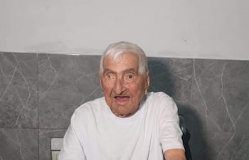 Canuto González, hombre mayor canoso, sonríe sentado frente a una mesa con mantel colorido en un hogar acogedor.