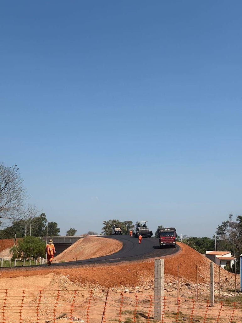 Cinco trabajadores en uniformes naranjas operan maquinaria en obra de la ruta PY02, bajo un cielo despejado.