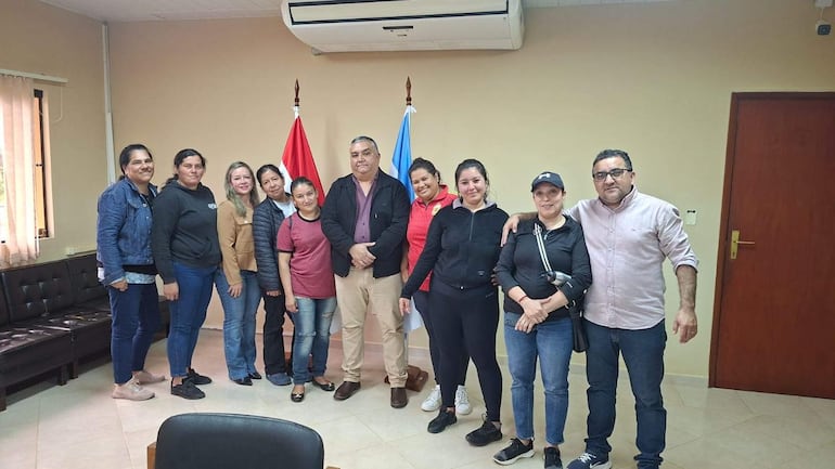 Diez personas de pie en sala de reuniones, con atuendos casuales y deportivas, en un ambiente con banderas de Paraguay y Argentina.