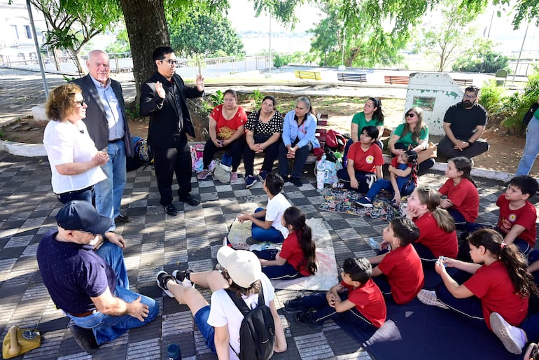 Grupo de personas, incluidos niños y adultos, en la Plaza de los Desaparecidos, algunos con camisetas rojas, escuchando atentamente a un orador en el centro.