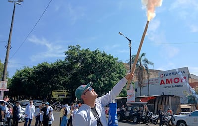 Hombre con bata blanca y gorro verde alzado con antorcha, rodeado de personas en manifestación festiva en la calle.
