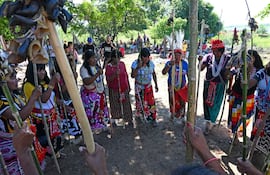 Mujeres de la comunidad Maka, vestidas con indumentarias coloridas, sostienen bastones en un entorno natural durante una celebración.