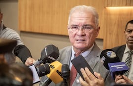 Hombre de pie en un podio hablando, vestido con traje. Audiencia sentada, escuchando atentamente y algunos con teléfonos móviles.