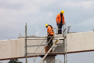 Dos trabajadores en el andamio, con cascos amarillos y chaquetas naranjas, trabajan en una estructura elevada de concreto bajo un cielo nublado.