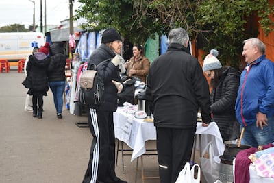 Mujeres con abrigos conversan en un mercado al aire libre, rodeadas de productos y un ambiente urbano fresco y nublado.