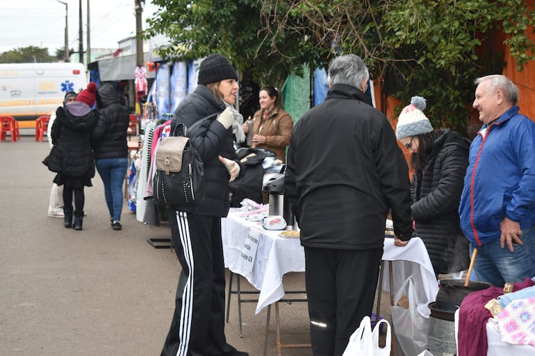 Mujeres con abrigos conversan en un mercado al aire libre, rodeadas de productos y un ambiente urbano fresco y nublado.