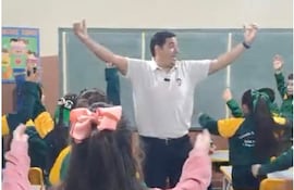 Leonardo Escobar Salinas en camiseta blanca, cantando con niños en una aula decorada, todos muestran entusiasmo y alegría.