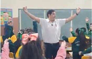 Leonardo Escobar Salinas en camiseta blanca, cantando con niños en una aula decorada, todos muestran entusiasmo y alegría.