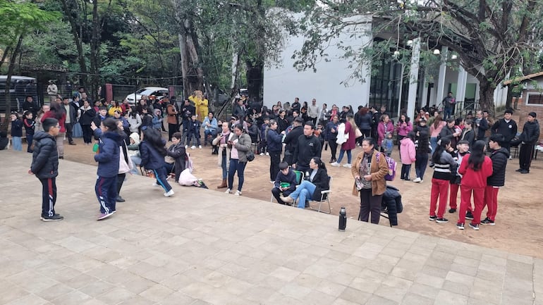 Grupo de estudiantes en chaquetas oscuras y pantalones deportivos, interactuando en un evento al aire libre rodeados de público variado.