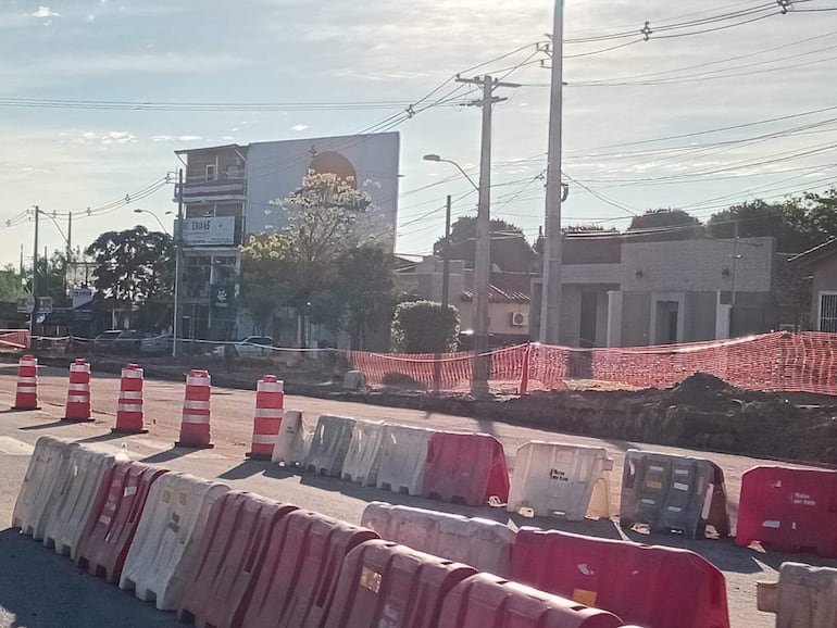 Escena de obras viales sin personas, con conos y bloques de hormigón, en un entorno urbano.