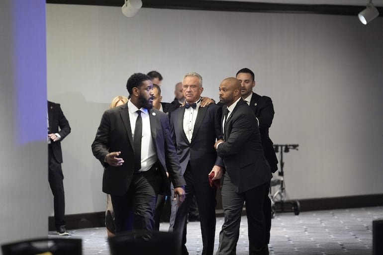 El secretario de Salud y Servicios Humanos, Robert Kennedy Jr., es evacuado por agentes del orden durante la cena de la Asociación de Corresponsales de la Casa Blanca en el Hotel Washington Hilton en Washington, D.C., el 25 de abril de 2026. El presidente Trump y la primera dama Melania Trump fueron evacuados previamente del evento tras un tiroteo dentro del hotel.