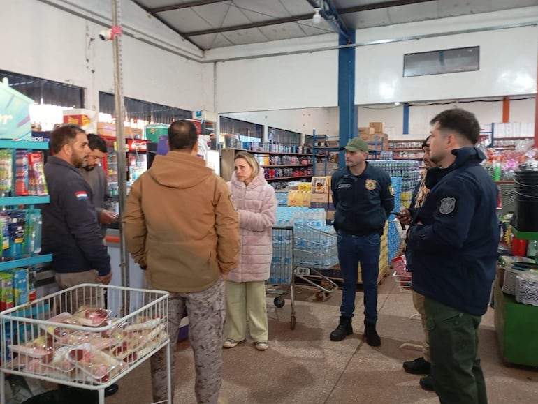 Tres hombres y tres mujeres conversan en supermercado, uno de los hombres lleva chaqueta con bandera paraguaya.