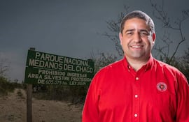 José Rodríguez sonríe frente al cartel del Parque Nacional Médanos del Chaco, vestido con camisa roja y emblema visible en el pecho.