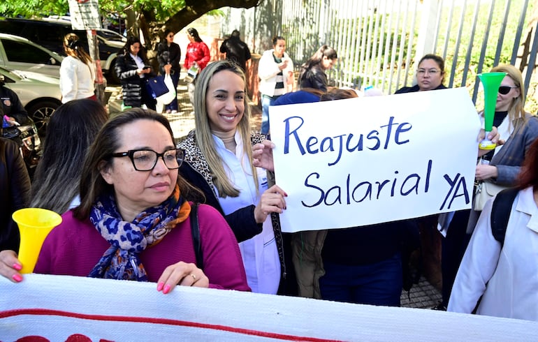 Mujeres en protesta, una con camiseta blanca y chal animal, otra sonriente sosteniendo un cartel de 'Reajuste Salarial YA'.