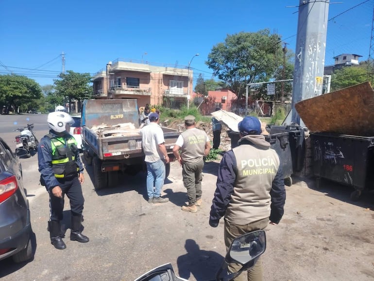 Dos agentes de Policía Municipal en chalecos claros conversan mientras observan un camión de carga en la calle con residuos.