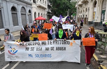 Participantes de la marcha sostienen pancartas coloridas, con el lema 'MI CUERPO, MI TERRITORIO NI SE USA NI SE ABUSA', en un ambiente urbano.