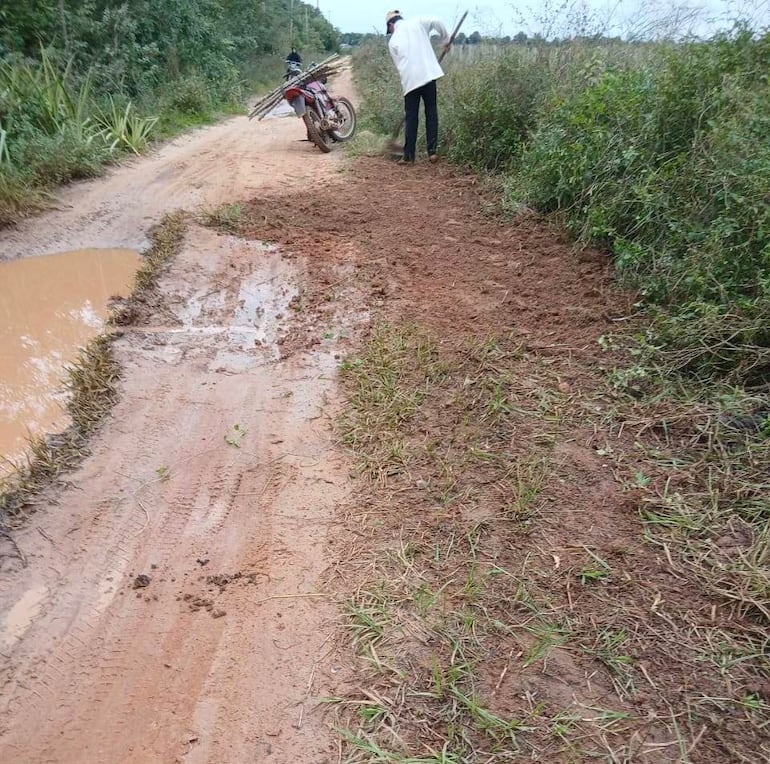 Hombre de espaldas con abrigo blanco y ropa oscura trabaja en camino de tierra con una herramienta en entorno rural.