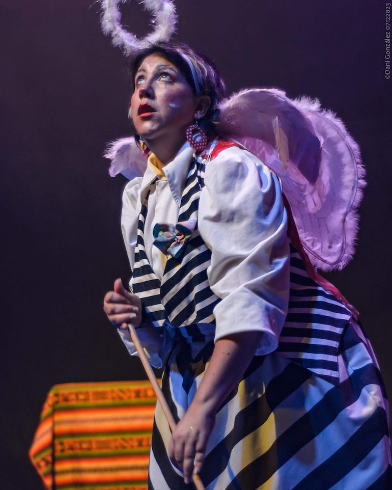 Mujer con atuendo de ángel, camiseta blanca con rayas negras, bailando en un escenario oscuro.