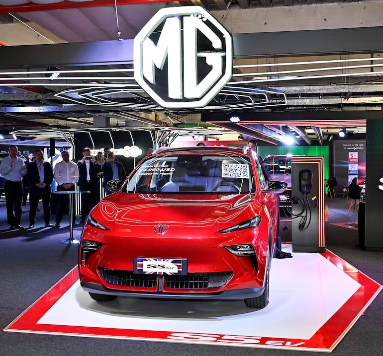 Vehículo eléctrico MG SS EV en pedestal con hombres en camisas y chaquetas observando atentamente la presentación.