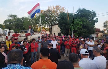 Grupo de personas reunidas en el exterior, con un hombre de traje oscuro dirigiendo la conversación, mientras ondea una bandera paraguaya.