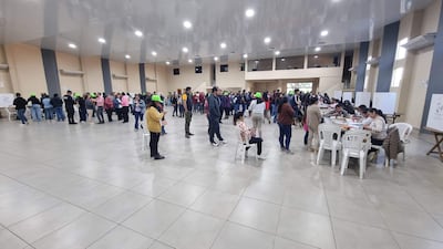 Asistentes con gorras verdes en fila, algunos revisan documentos y otros usan teléfonos móviles en un ambiente colaborativo.