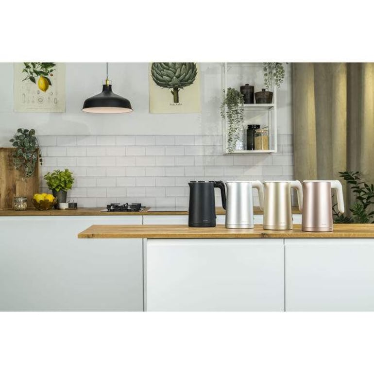Cocina moderna con tres hervidores eléctricos en negro, plateado, dorado y rosado, rodeados de decoración natural y estante con frascos.