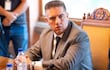 Hombre en traje gris oscuro y corbata blanca sentado en mesa de reunión, mirando atentamente a su interlocutor.