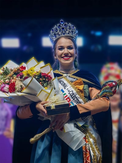 Anabel Sitzmann Hahn sonríe con corona y ramo de flores, vestida en traje tradicional, en un ambiente festivo.
