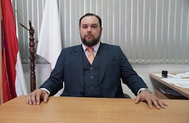 Pablo José Morínigo Cáceres sentado frente a un escritorio, vestido con traje azul y corbata naranja, expresión seria en una oficina con banderas.