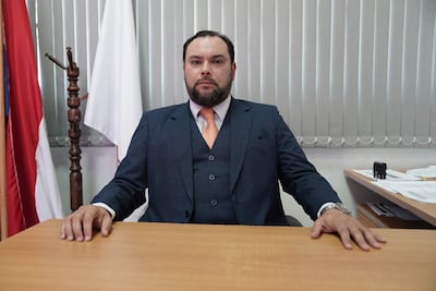 Pablo José Morínigo Cáceres sentado frente a un escritorio, vestido con traje azul y corbata naranja, expresión seria en una oficina con banderas.