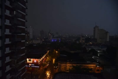 Vista de ciudad en noche oscura, con edificio rojo iluminado y cielo nublado. Sin personas presentes.
