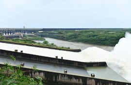 Vista panorámica de represa de Itaipú con compuertas abiertas y fuerte caudal de agua, en un entorno natural con vegetación.