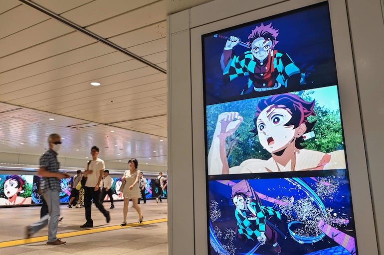 Personas caminan junto a carteles digitales que anuncian el próximo lanzamiento del videojuego “Demon Slayer: Kimetsu no Yaiba – The Hinokami Chronicles 2”, a lo largo de un pasillo dentro de una estación de tren en el centro de Tokio, el 29 de julio de 2025.