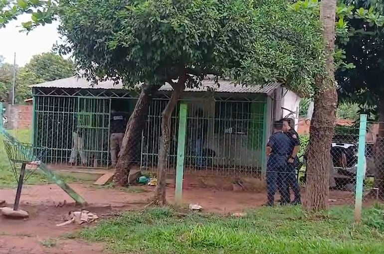 Dos agentes en uniforme oscuro conversan en un exterior tranquilo mientras un tercero está dentro de una vivienda.