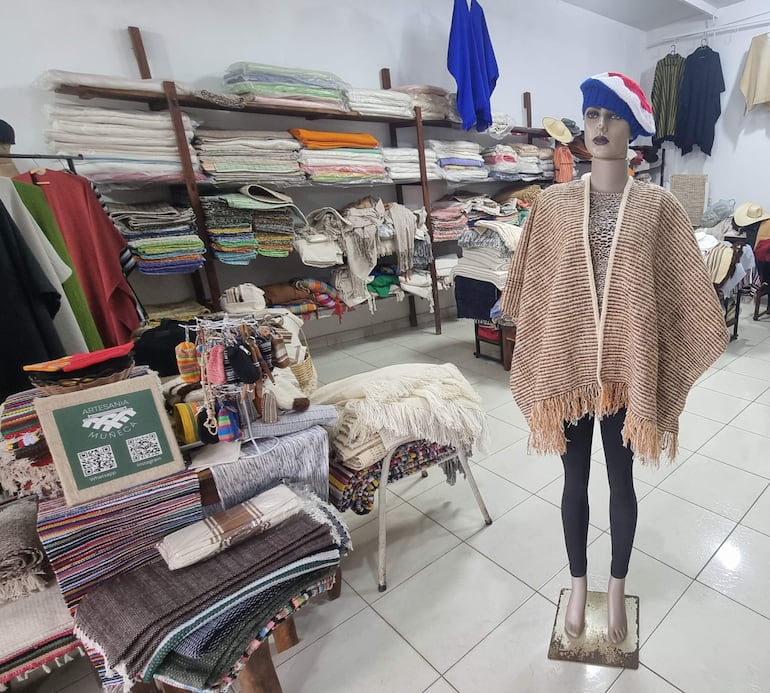 Maniquí con poncho de rayas y gorro de lana en un local lleno de artesanías paraguayas coloridas.
