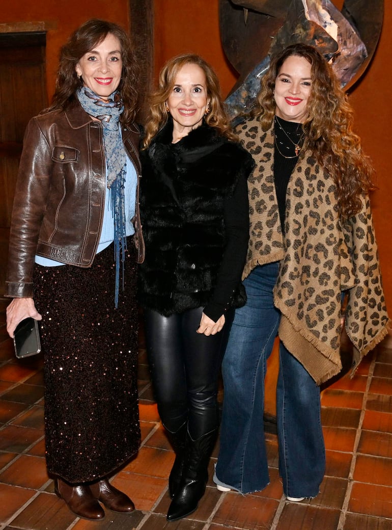 Mujeres sonrientes, una con chaqueta de piel negra, otra en suéter negro, y la última con chaqueta de cuero marrón.