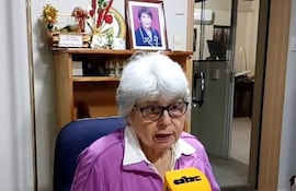 Corina Falcón, mujer mayor con gafas y cabello canoso, habla frente a un micrófono en un ambiente profesional decorado.