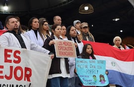 Mujer sostiene cartel '¡Los médicos especialistas renunciaron!' mientras médicos con batas blancas protestan en un espacio público.