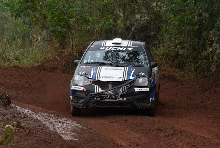 Automóvil de rally número 88, con diseño negro y azul, atraviesa curva de barro en entorno natural.