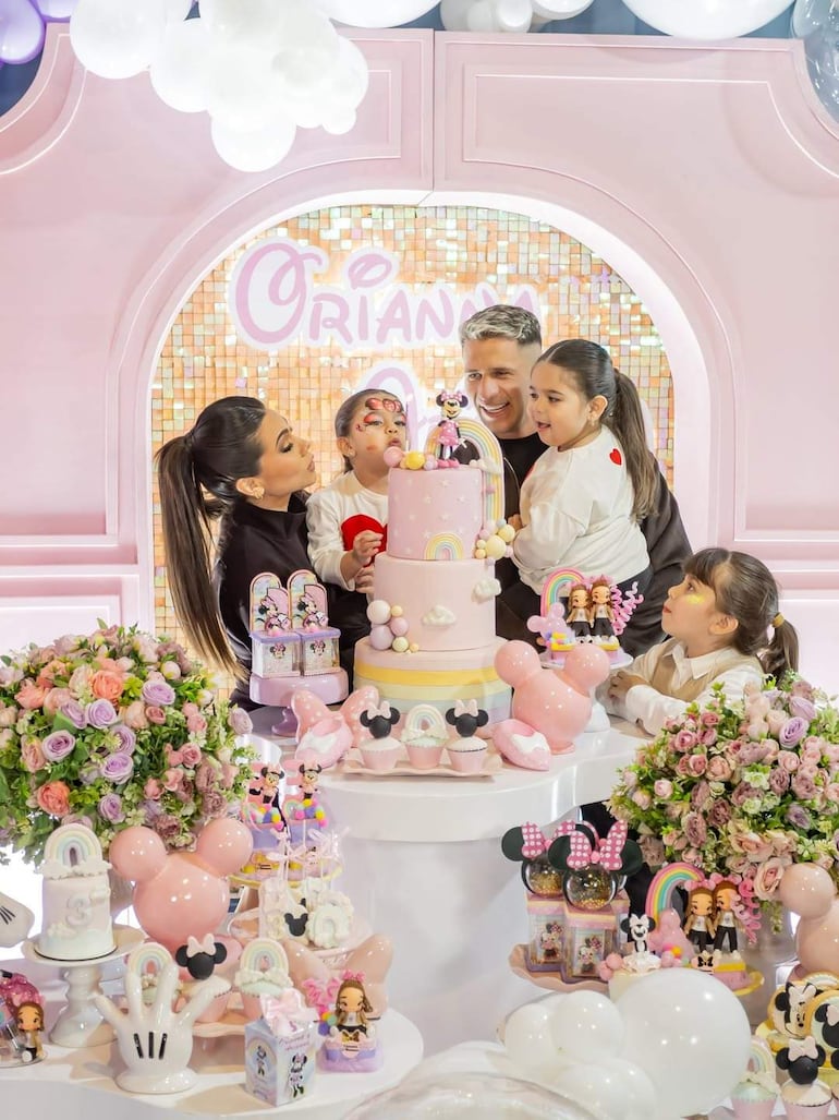 Niños con expresiones de alegría rodean la torta de cumpleaños de Oriana, decorada con temas de arcoíris y Minnie Mouse.