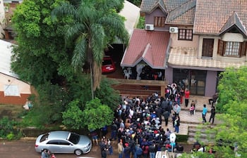 Multitud de más de 100 personas frente a casa, algunas con abrigos, ambiente de expectativa y atención hacia un orador.