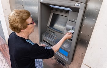 Una jubilada retira dinero de un cajero automático.
