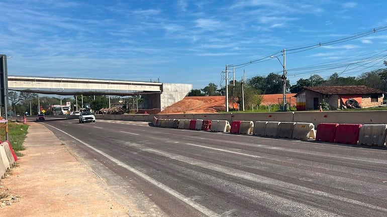 Escena de una carretera en construcción con un puente elevado y barreras de concreto rodeando el área de trabajo.