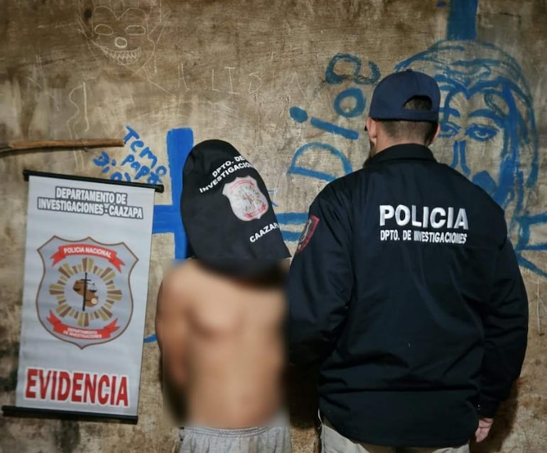 Sospechoso con torso desnudo y capuchón rodeado por agente de policía con chaqueta negra en un ambiente de investigación.