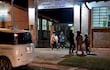 Cinco padres se reúnen cerca de la escuela con expresión de preocupación, observando las instalaciones iluminadas por la noche.