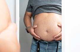 Hombre con sobrepeso se mira la panza en un espejo.