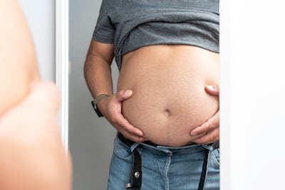 Hombre con sobrepeso se mira la panza en un espejo.